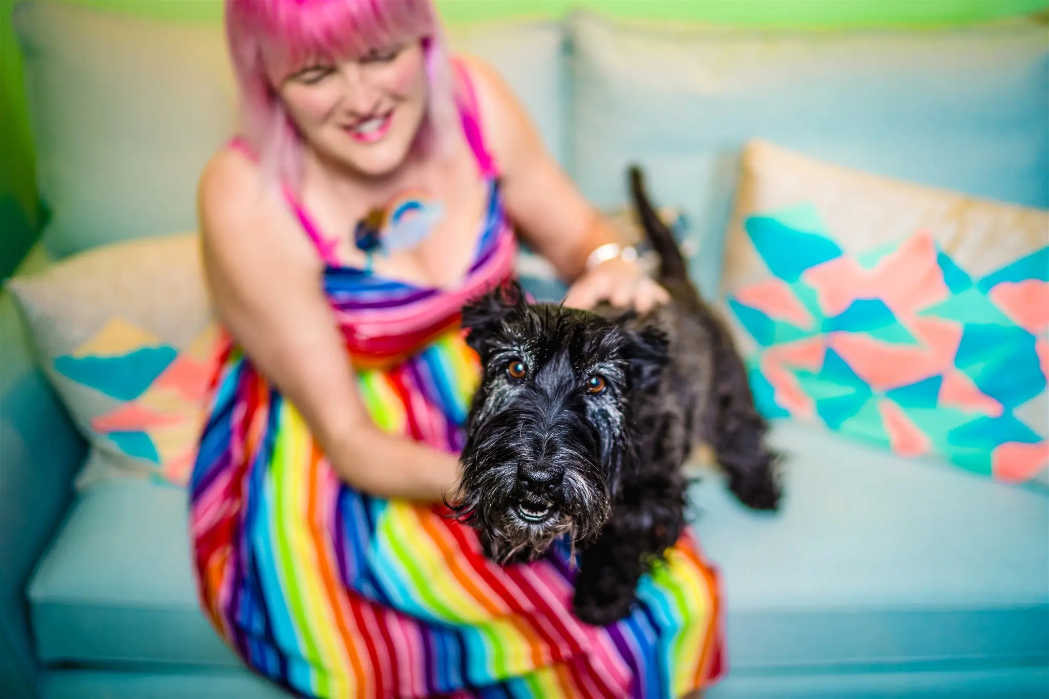 Laura_Keasley_HEADSHOTS-3 Laura Kelsey with bright pink hair smiling while holding her black dog Clementine.